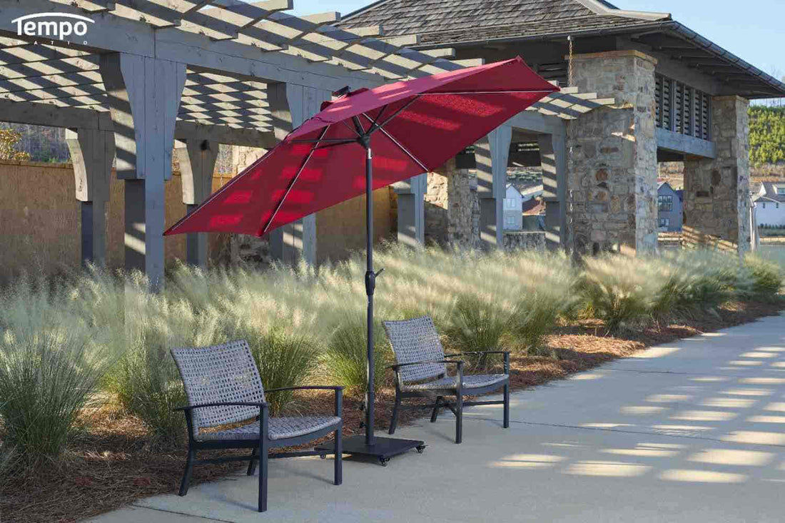 Choosing an umbrella over fixed shade structures with a red patio umbrella beside wicker chairs on a walkway. 