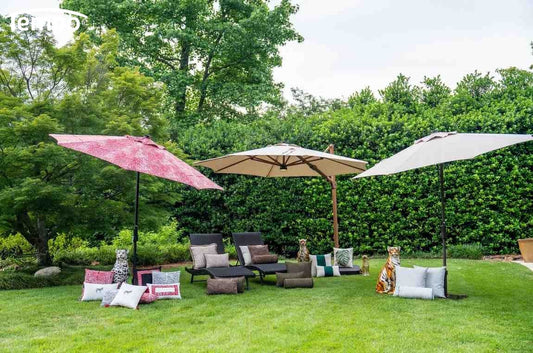A garden seating area comparing portable shade with umbrellas in pink and beige over lounge chairs on green lawn.