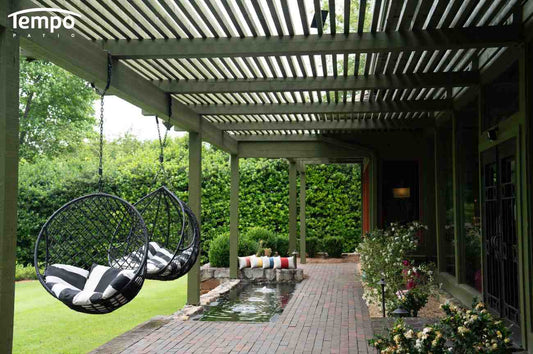 Patio umbrellas vs pergolas comparison featuring a wood pergola with hanging egg chairs over a brick patio and garden