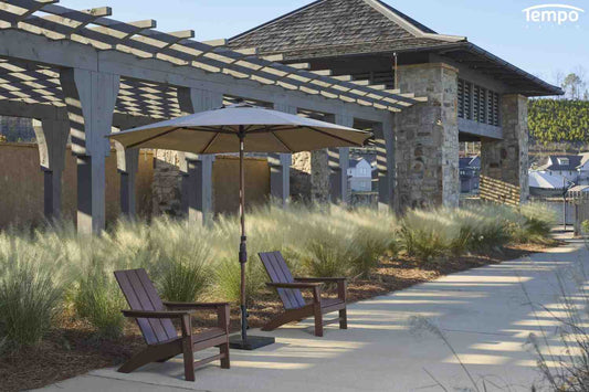Umbrella vs canopy comparison guide featuring a center pole patio umbrella beside two chairs near a waterfront 