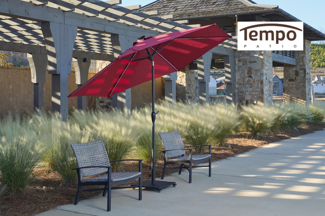 Difference between umbrellas and permanent shade with a red patio umbrella beside a stone pergola structure.
